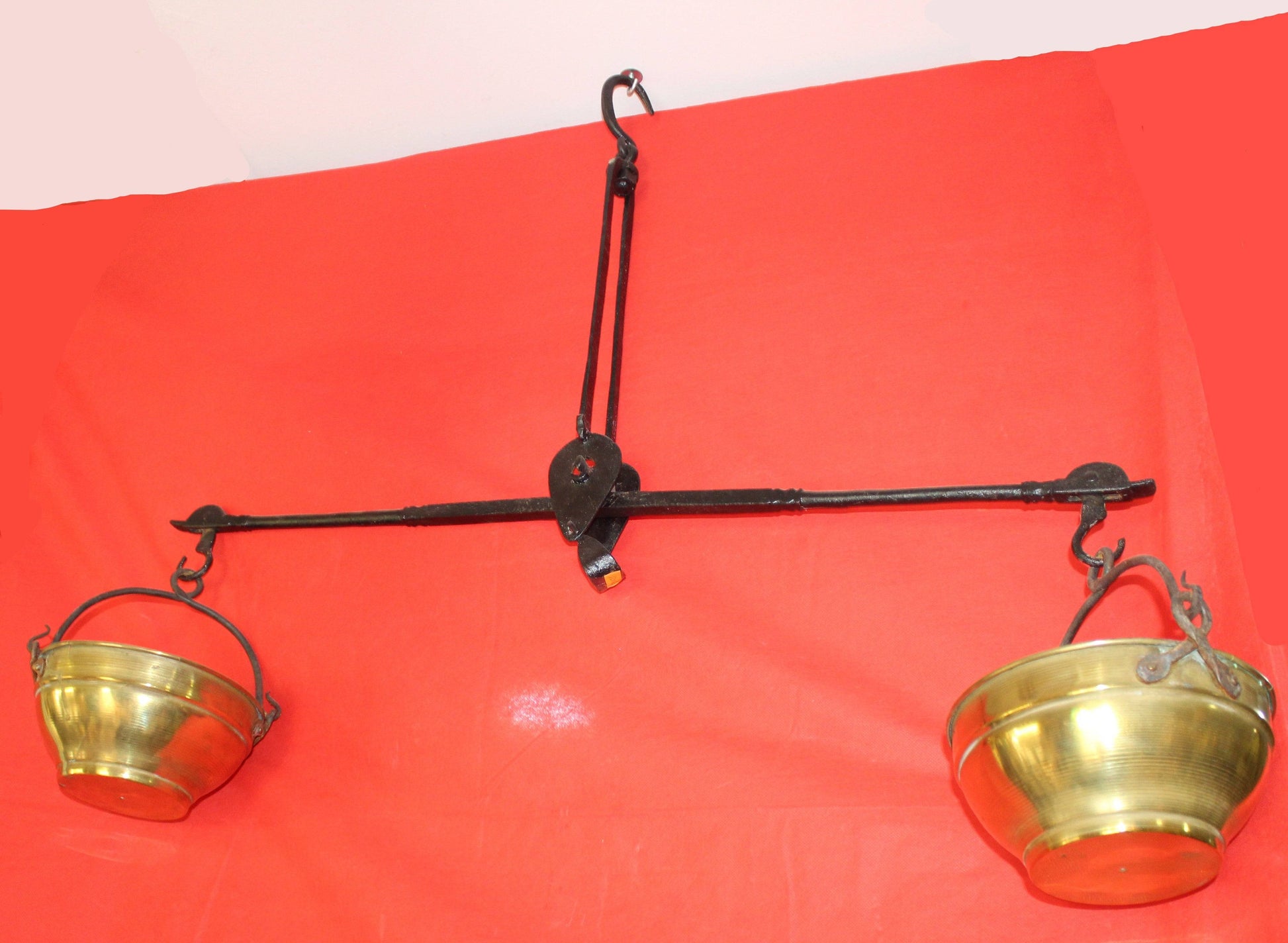 Balanza de hierro con cuencos de metal dorado sobre fondo rojo, decoración vintage ideal para el hogar. Excelente calidad y estilo antiguo.